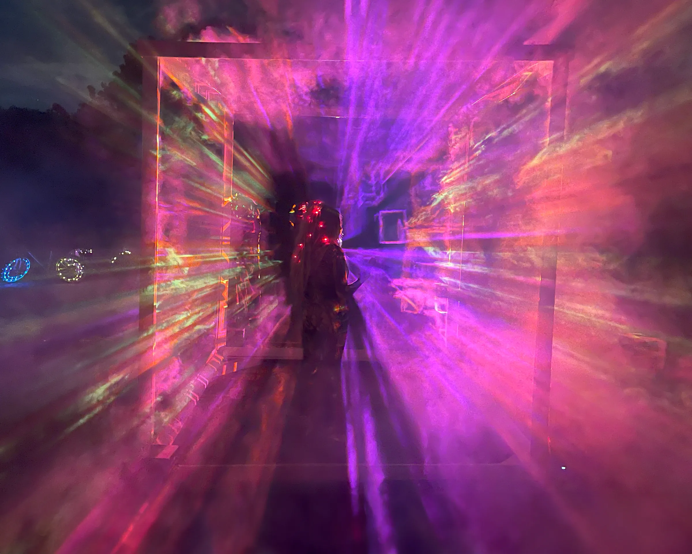 Pink and purple light beams radiate outward around a silhouetted figure with tiny lights woven into their hair.