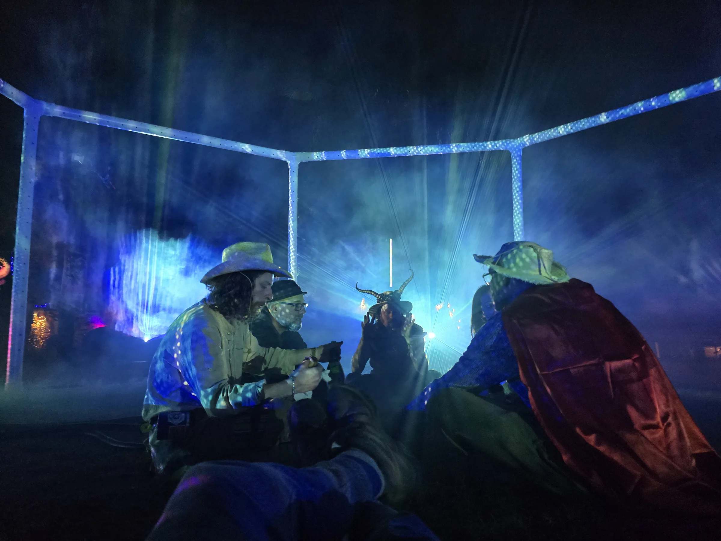 The Octagon at night: an octagonal truss structure filled with fog and converging beams of projected light