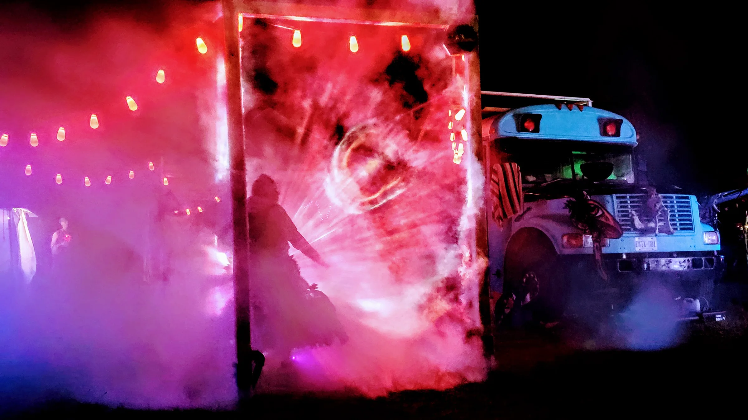 The wooden portal glows deep red with a circular light pattern, a silhouetted figure in a flowing skirt inside, a bus parked beside it.