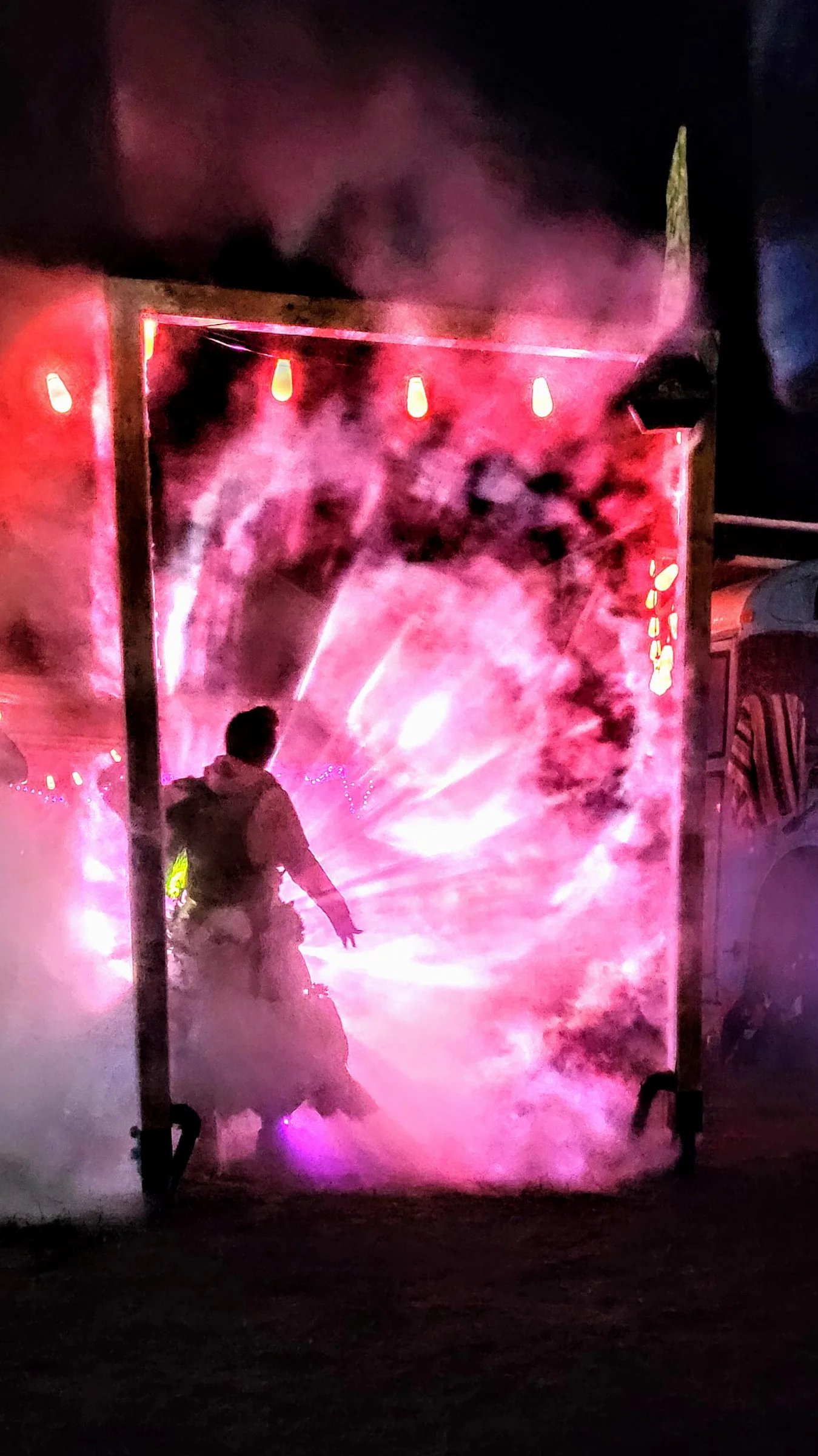 A silhouetted figure in a full skirt stands inside the wooden portal frame, swirling magenta light forming a vortex pattern around them.