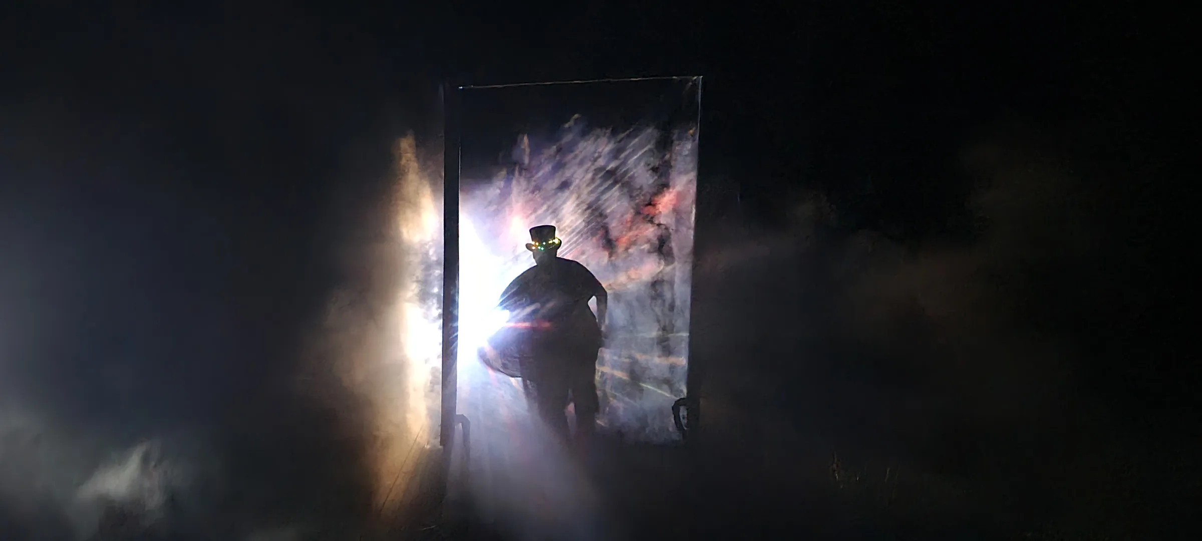 A silhouetted figure in a top hat with tiny lights stands in the doorway, framed by a burst of white light and pink-streaked fog.